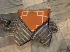 an orange and blue pillow laying on top of a bed next to a gray blanket