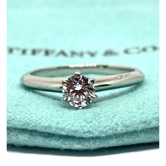 a diamond engagement ring sitting on top of a blue velvet pad with the words tiffany & co written below it