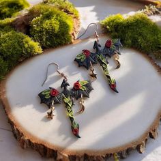 the earrings are decorated with red flowers and black leaves, on top of a piece of wood