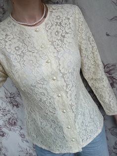 This vintage blouse from the 70s is crafted from cream white lace, offering a delicate and feminine aesthetic. The intricate lace design is complemented by elegant pearl buttons, adding a touch of sophistication and classic charm. Perfect for both casual and formal occasions, this women's shirt embodies the timeless appeal of 70s fashion with its detailed craftsmanship and elegant silhouette. The combination of lace and pearl accents creates a versatile piece that exudes romantic elegance. - Goo Spring Lace For Formal Occasions, Elegant Button-up Wedding Blouse, Classic Fitted Blouse With Pearl Buttons, Formal Lace Tops With Buttons, Lace Tops With Buttons For Formal Occasions, Formal Blouse With Pearl Buttons, Classic White Blouse With Pearl Buttons, Classic Formal Blouse With Pearl Buttons, Elegant Long Sleeve Blouse With Pearl Buttons