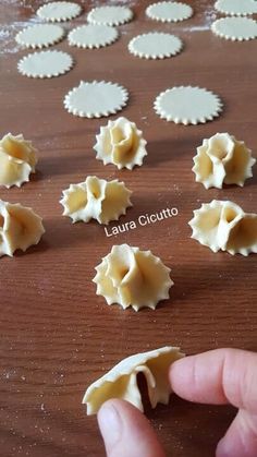 someone is making ravioli on a wooden table with their fingers pointing at the pasta