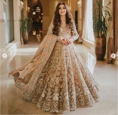 a woman in a gold and white bridal gown posing for the camera with her hands on her hips