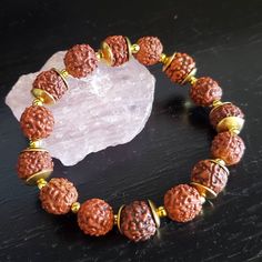 "This beautiful bracelet is inspired by the bracelets made to decorate deities at Hindu temples. The golden beads highlight the natural beauty of the Genuine Rudraksha beads. Matching mala necklace is also available.  Available in 3 sizes To learn more about the benefits of wearing Rudraksha watch this video I made for my YouTube channel:  https://youtu.be/68NcJy0kaPg Wearing Rudraksha strongly connects us to Shiva Himself. Meditating with Rudraksha strengthens the spiritual quality of our meditations, drawing blessings from Rudra. The Rudraksha seeds used in this bracelet are known as a \"Panch Mukhi Rudraksha,\" meaning that they have five faces. Each face is connected to one syllable of the sacred mantra \"Namah Shivaya.\" All Gemstone and Crystals information is historical or anecdotal Handmade Spiritual Mala, Spiritual Hand Wrapped Beaded Bracelets For Festival, Spiritual Meditation Bracelets, Spiritual Hand-wrapped Beaded Bracelets For Festivals, Spiritual Round Beads Bracelets For Meditation, Handmade Spiritual Beaded Bracelets For Meditation, Spiritual Brown Beaded Bracelets For Rituals, Spiritual Brown Beaded Bracelets, Spiritual Hand-strung Beaded Bracelets For Rituals