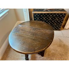 a round wooden table sitting on top of a carpeted floor next to an old suitcase