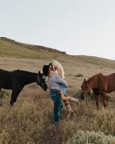 a woman is hugging her dog while two horses graze in the field