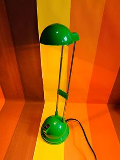 a green table lamp sitting on top of a wooden floor next to an orange and yellow wall