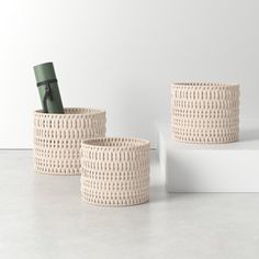 three woven baskets sitting next to each other on top of a white surface with a bottle in the middle