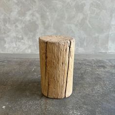 a small wooden stump sitting on top of a cement floor next to a gray wall