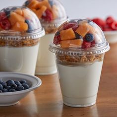 yogurt cups with fruit and granola in them sitting on a wooden table