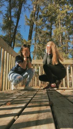 two people kneeling down on a wooden deck with their hands in the air and trees behind them