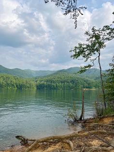 a lake surrounded by trees and mountains under a cloudy sky