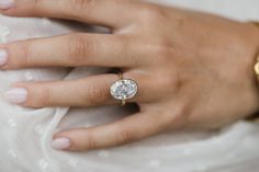 a woman's hand with a diamond ring on her left hand, wearing a white dress