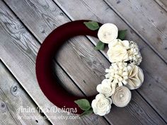 a wreath with white flowers and green leaves sitting on top of a wooden floor next to a wall