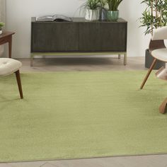 a green rug in a living room with two chairs and a plant on the wall