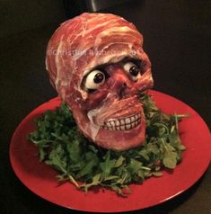 a red plate topped with meat covered in green leafy greens and an evil looking face