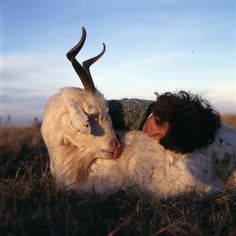 a woman laying on the ground next to a white animal with long horns and an antelope's head