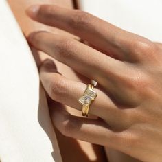 a woman's hand wearing a yellow gold ring with a square shaped diamond on it