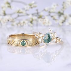 two gold wedding rings with green and white stones on the sides, one is in front of