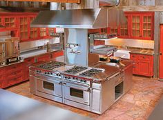 a kitchen with red cabinets and stainless steel stove top oven, range hood and sink