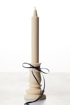 a white candle with a black ribbon tied around it on a table in front of a white background