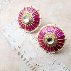 The centerpiece of these earrings features a resplendent Rani (Fuchsia Pink) Kundan, known for its deep and regal hue, making a bold statement that captivates all who behold it. Surrounding this radiant Kundan is a delicate Meenakari design, which adds an artistic touch to the piece. The Meenakari details are meticulously hand-painted with vivid enamels, showcasing a symphony of colors that harmoniously complement the vibrant pink. To enhance the overall charm, these earrings are elegantly frame Elegant Festive Plug Earrings, Festive Plug Earrings For Festivals, Elegant Purple Meenakari Jewelry, Pink Bridal Earrings For Festive Occasion, Fusion Style Bridal Earrings With Meenakari, Pink Fusion Style Formal Earrings, Elegant Purple Jewelry For Diwali, Traditional Pink Earrings For Formal Occasions, Elegant Purple Jewelry For Festivals