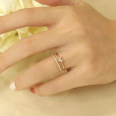 a woman's hand with a diamond ring on top of her finger and a flower in the background