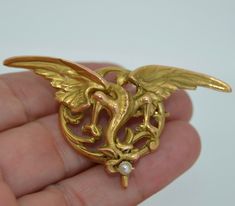 This is a very versatile piece. It can be adorned as a pendant, a brooch as well as a watch pin. It originates from France and is hallmarked with the French eagles head guarantying that it is 18K solid gold. This incredibly detailed puce dates from the 1890s-1910 (Art Nouveau Era). It is a rendering of a winged chimera (dragon or griffin). The griffin is in flight with a single round pearl braced in its mouth. This dragon has a wing span of 2.5 inches so it is not a tiny piece. The back of the p Gold Art Nouveau Brooch For Collectors, Art Nouveau Gold Brooch With Cabochon, Gold Locket Brooch For Collectors, Unique Gold Brooches With Cabochon, Unique Gold Brooch With Cabochon, Heirloom Pendant Brooches As Gifts, Unique Gold Pendant Brooches, French Art Nouveau, A Wing