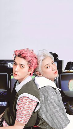 two young men sitting next to each other in front of televisions with pink hair