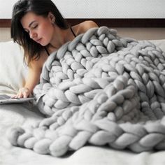 a woman laying in bed with a blanket on top of her and reading a book