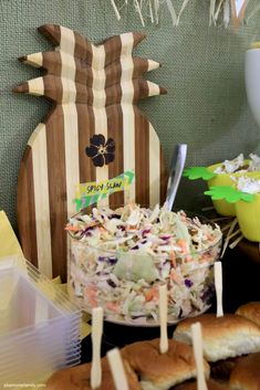 a table topped with lots of food next to a bowl of coleslaw and buns