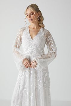 a woman is wearing a white dress with sheer sleeves and an intricate pattern on it