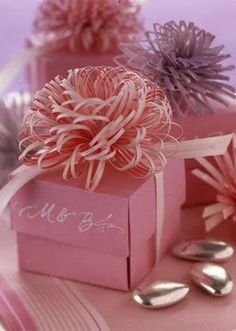 two pink boxes with flowers in them sitting on a table next to silver spoons