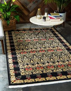 a black and gold area rug in front of a table with two plants on it