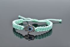 a green bracelet with an evil eye and hamsah charm on the end is shown