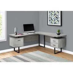 an office desk with two drawers and a computer monitor on top of it, in front of a gray wall