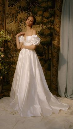 a woman in a white wedding dress standing next to a wall with flowers on it