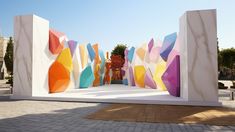 an outdoor sculpture with colorful shapes and trees in the backgroung, surrounded by brick pavers