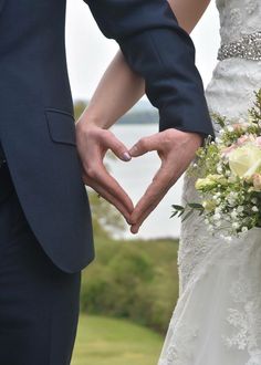 a bride and groom hold their hands in the shape of a heart