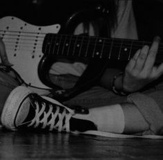 a person sitting on the floor with a guitar in their lap and one hand holding an electric guitar