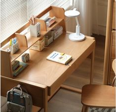 a wooden desk with a book, lamp and other items on it in front of a window