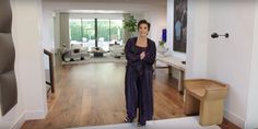 a woman standing in the middle of a living room with hardwood floors and white walls