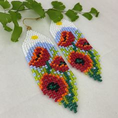 the beaded earrings are decorated with red and yellow flowers on white background next to green leaves