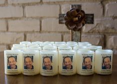 many candles with pictures of the same man are lined up on a table in front of a brick wall