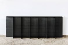 a black cabinet sitting in the middle of a room next to a white wall and floor