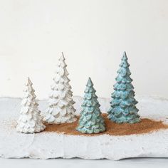 three small ceramic christmas trees sitting on top of a white table cloth next to each other