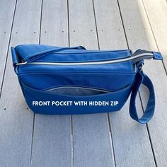 the front pocket with hidden zip is shown on a wooden deck and has a blue bag attached to it