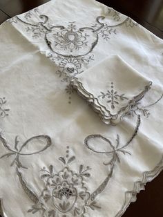 two napkins on top of a white table cloth with silver embroidered designs and bows