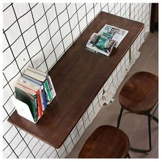 two wooden stools sitting next to a table with books on it and a magazine rack