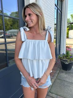 This flowy top features tied bows on the shoulders with blue stitching, adding a touch of playful charm to your look. Embrace effortless style with this versatile and comfortable top.   Model is 5’2″ with a 25″ waist, 31″ hips and a 32″ Bust and is wearing a small. Fits true to size 100% Polyester Linning 100% Polyester Chic Spring Tops With Bow Straps, Spring Sleeveless Tops With Bow, Chic Tops With Bow Straps For Day Out, Casual Sleeveless Top With Bow Straps, Trendy Sleeveless Top With Bow, Summer Tops With Bow Straps, Summer Tops With Bow Detail, Chic Vacation Tops With Knotted Straps, Spring Brunch Tops With Tie Straps