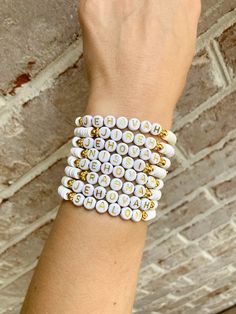 a woman's hand wearing a white and gold beaded bracelet with letters on it